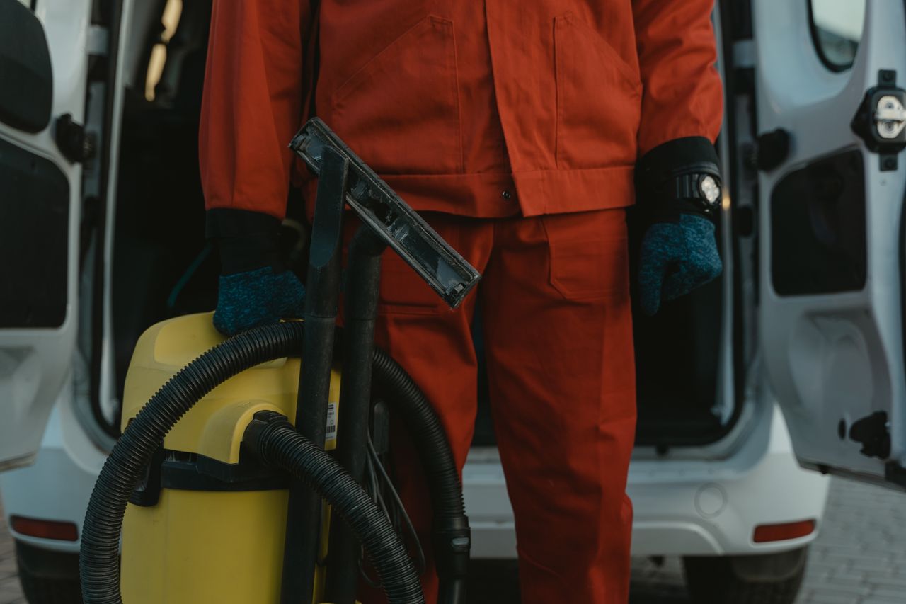 services-03 A professional cleaner in a red uniform standing by a van with a vacuum, prepared to provide service.